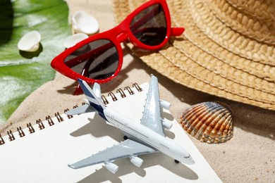 Photo of Time for summer vacation. Toy plane, notebook, green leaf and beach accessories on sand, closeup