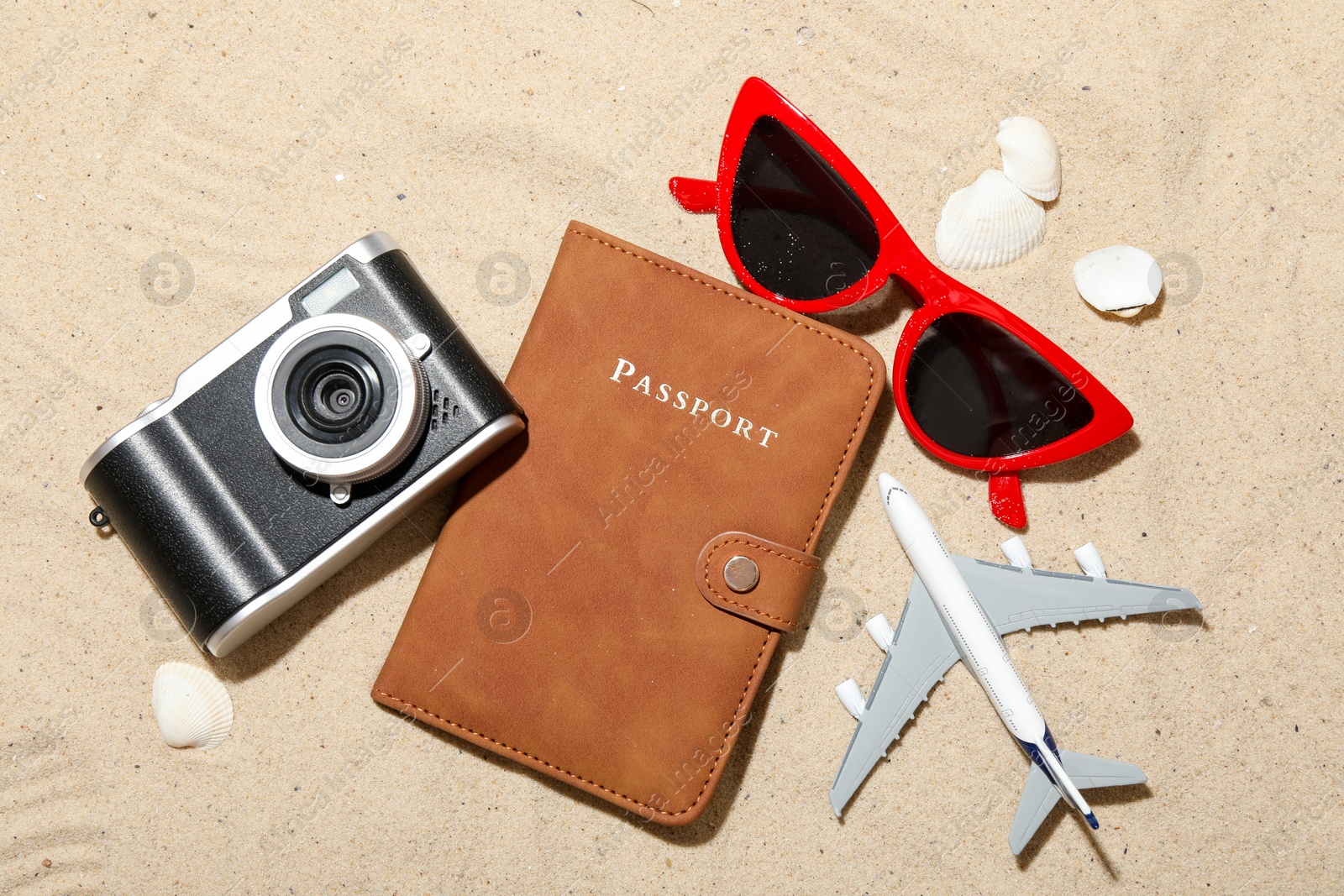 Time for summer vacation. Passport, camera, toy plane, sunglasses and seashells on sand, flat lay Photo of Time for summer vacation. Passport, camera, toy plane, sunglasses and seashells on sand, flat lay