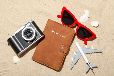 Photo of Time for summer vacation. Passport, camera, toy plane, sunglasses and seashells on sand, flat lay