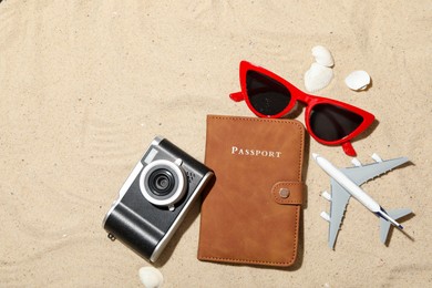 Photo of Time for summer vacation. Passport, camera, toy plane, sunglasses and seashells on sand, flat lay. Space for text