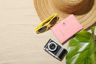 Photo of Time for summer vacation. Camera, passport, green leaf and beach accessories on sand, flat lay. Space for text