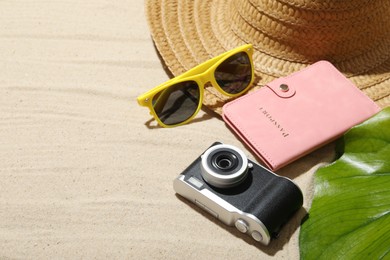 Photo of Time for summer vacation. Camera, passport, green leaf and beach accessories on sand, closeup. Space for text