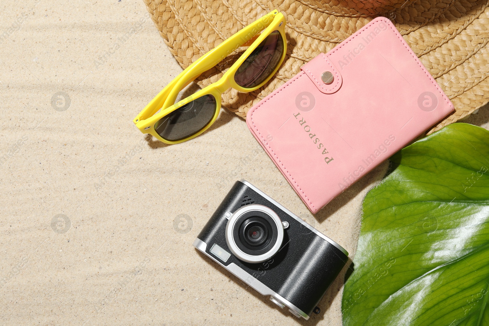 Photo of Time for summer vacation. Camera, passport, green leaf and beach accessories on sand, flat lay. Space for text