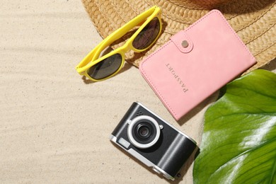 Photo of Time for summer vacation. Camera, passport, green leaf and beach accessories on sand, flat lay. Space for text