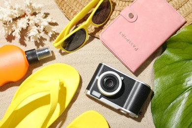 Photo of Time for summer vacation. Camera, passport, sunscreen, green leaf and beach accessories on sand, flat lay