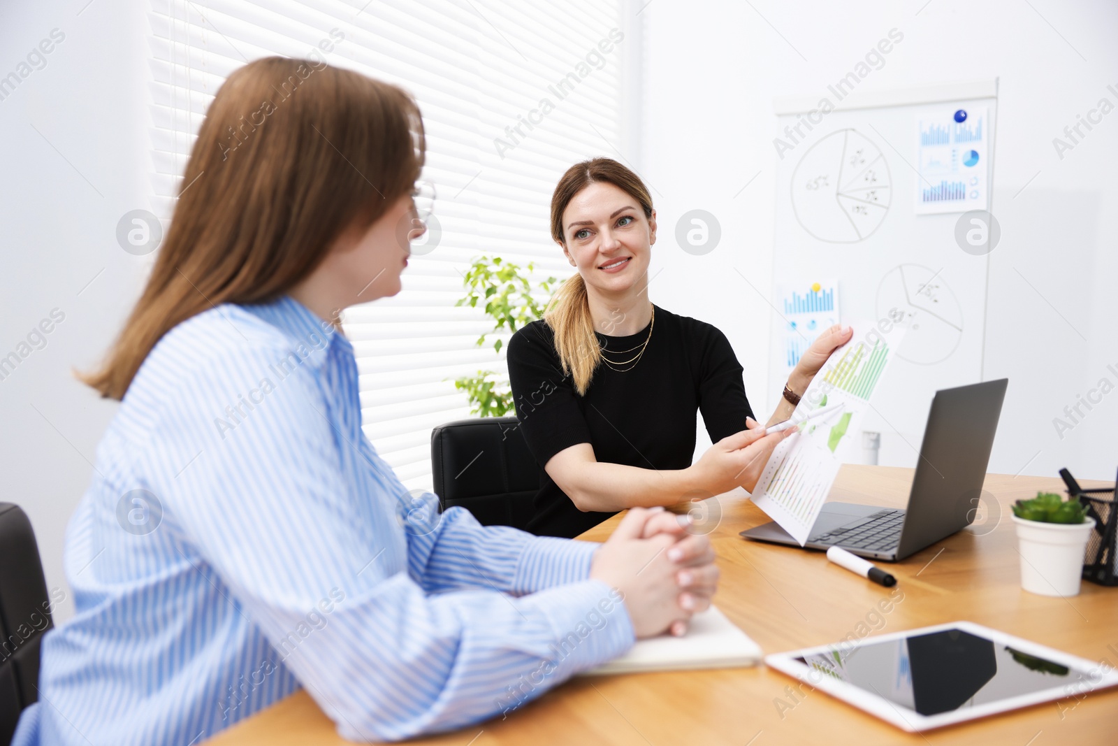 Business coach working with woman at wooden table in office Photo of Business coach working with woman at wooden table in office