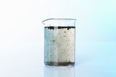 Photo of Glass beaker with dirty water on mirror surface