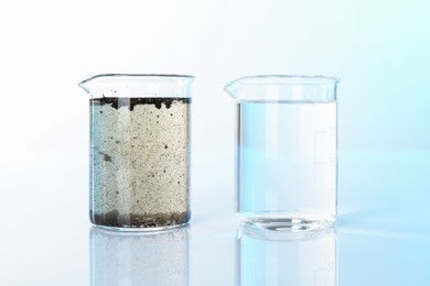 Photo of Glass beakers with clean and dirty water on mirror surface