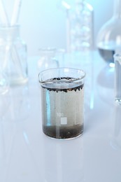 Photo of Glass beaker with dirty water and other glassware on mirror surface, closeup