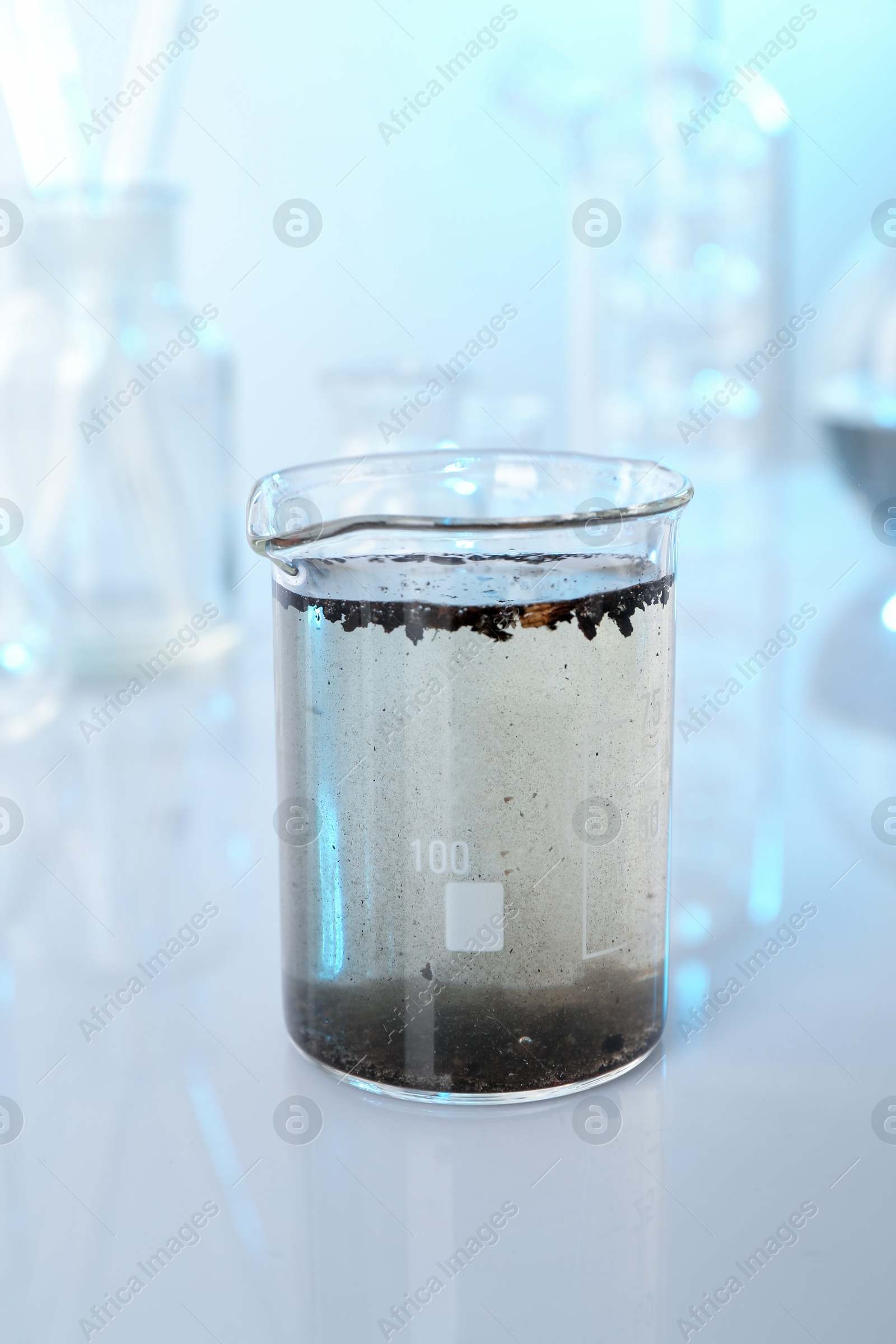 Photo of Glass beaker with dirty water and other glassware on mirror surface, closeup