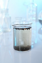 Photo of Glass beaker with dirty water and other glassware on mirror surface, closeup