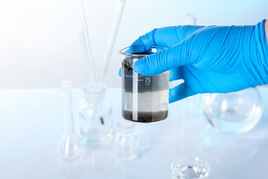 Photo of Scientist holding beaker with dirty water and other glassware against white background, closeup