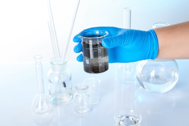 Photo of Scientist holding beaker with dirty water and other glassware against white background, closeup