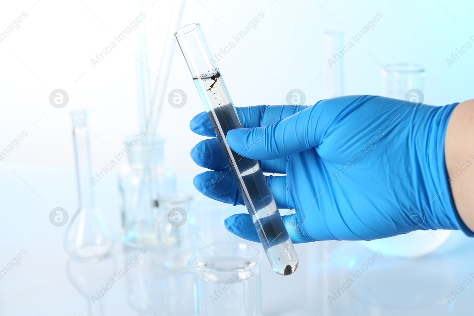 Photo of Scientist holding test tube with dirty water and other glassware against white background, closeup