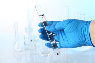 Photo of Scientist holding test tube with dirty water and other glassware against white background, closeup