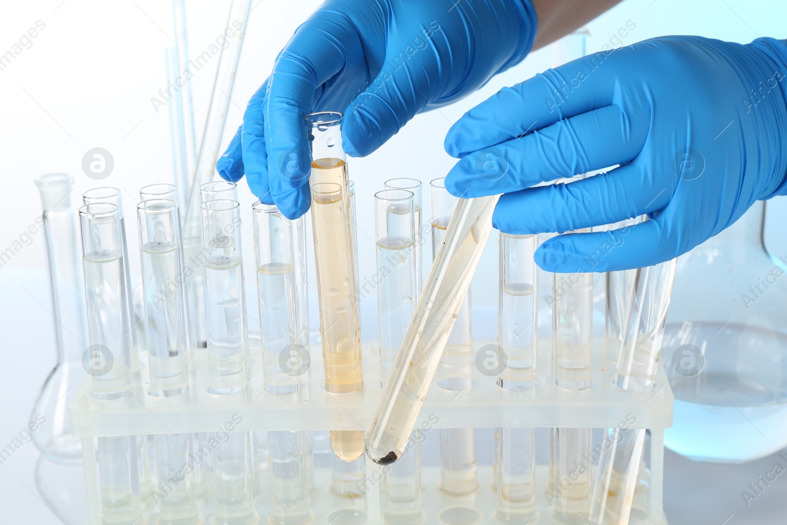 Photo of Examination of water quality. Scientist with test tubes of samples at table against light background, closeup