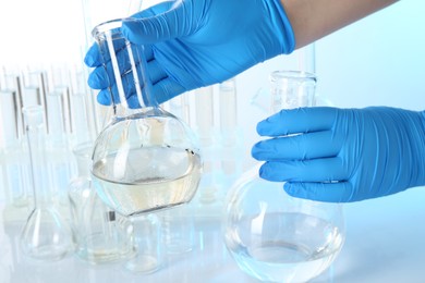 Photo of Scientist with flasks of dirty and clean water at table against light background, closeup