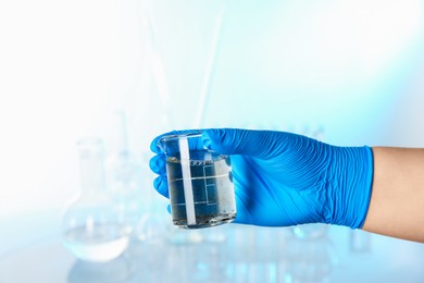 Photo of Scientist holding beaker with dirty water against blurred background, closeup