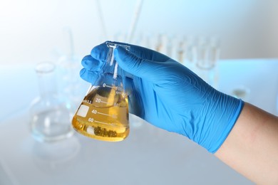 Photo of Scientist holding flask with dirty water against blurred background, closeup