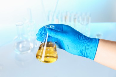 Photo of Scientist holding flask with dirty water against blurred background, closeup