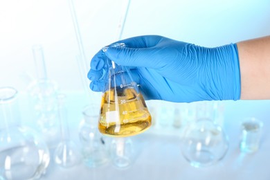Photo of Scientist holding flask with dirty water against blurred background, closeup