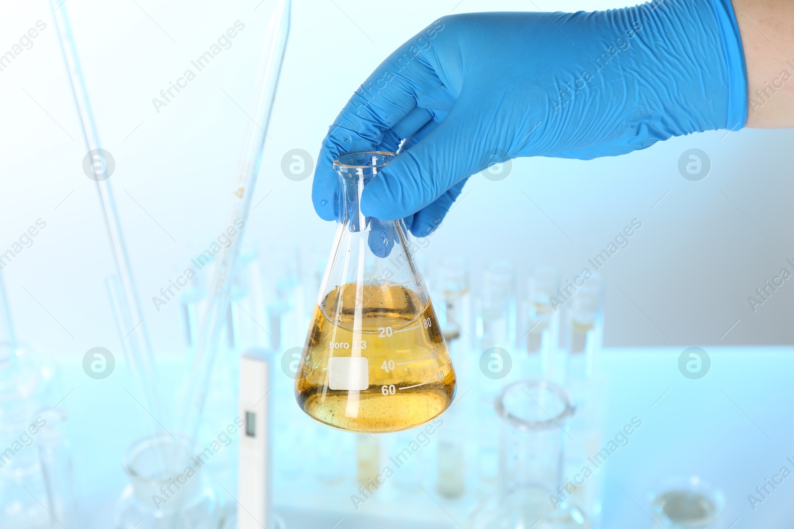 Photo of Scientist holding flask with dirty water against blurred background, closeup