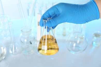 Photo of Scientist with flask of dirty water at table against blurred background, closeup
