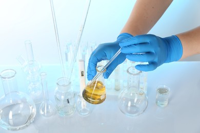 Photo of Examination of water quality. Scientist taking sample from flask at table against light background, closeup