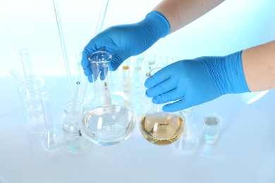 Photo of Scientist with flask of dirty water at table against light background, closeup