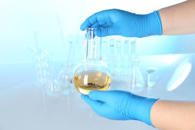 Photo of Scientist with flask of dirty water at table against light background, closeup