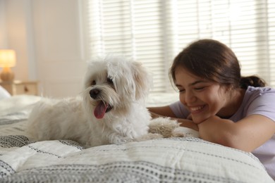 Photo of Happy teenage girl with cute Maltese dog on bed at home