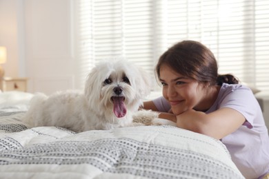 Photo of Happy teenage girl with cute Maltese dog on bed at home