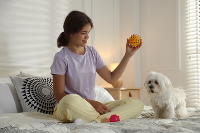 Photo of Happy teenage girl playing with cute Maltese dog on bed at home