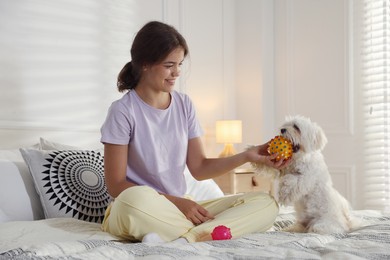 Photo of Happy teenage girl playing with cute Maltese dog on bed at home
