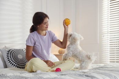 Photo of Happy teenage girl playing with cute Maltese dog on bed at home