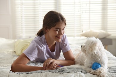 Photo of Happy teenage girl with cute Maltese dog on bed at home