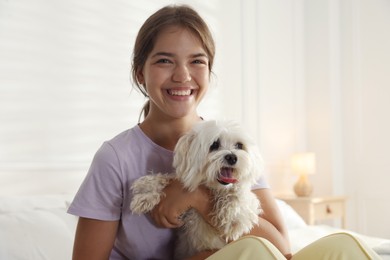Photo of Happy teenage girl with cute Maltese dog on bed at home