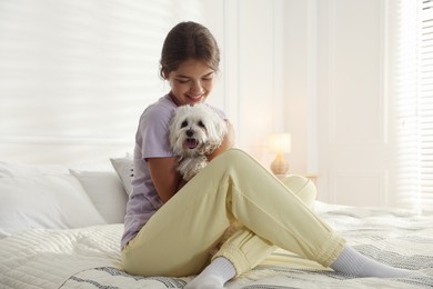 Photo of Happy teenage girl with cute Maltese dog on bed at home