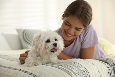 Photo of Happy teenage girl with cute Maltese dog on bed at home
