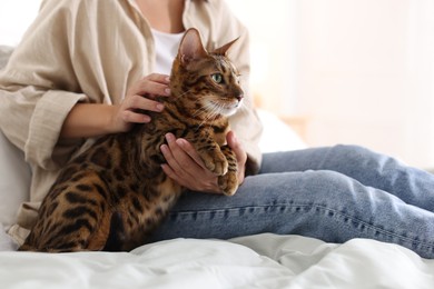 Photo of Woman with cute Bengal cat on bed at home, closeup. Adorable pet