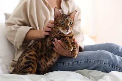 Photo of Woman with cute Bengal cat on bed at home, closeup. Adorable pet