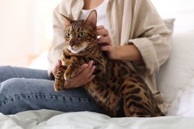 Photo of Woman with cute Bengal cat on bed at home, closeup. Adorable pet
