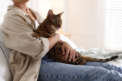 Photo of Woman with cute Bengal cat on bed at home, closeup. Adorable pet