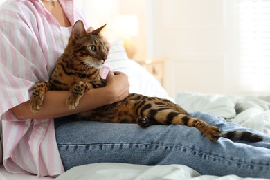 Photo of Woman with cute Bengal cat on bed at home, closeup. Adorable pet