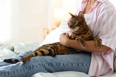 Photo of Woman with cute Bengal cat on bed at home, closeup. Adorable pet