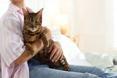 Photo of Woman with cute Bengal cat on bed at home, closeup. Adorable pet