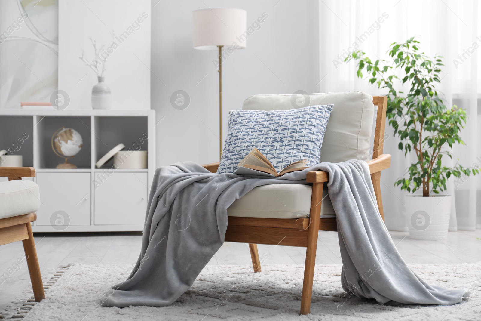 Photo of Comfortable armchair with book, pillow and blanket in living room. Interior design