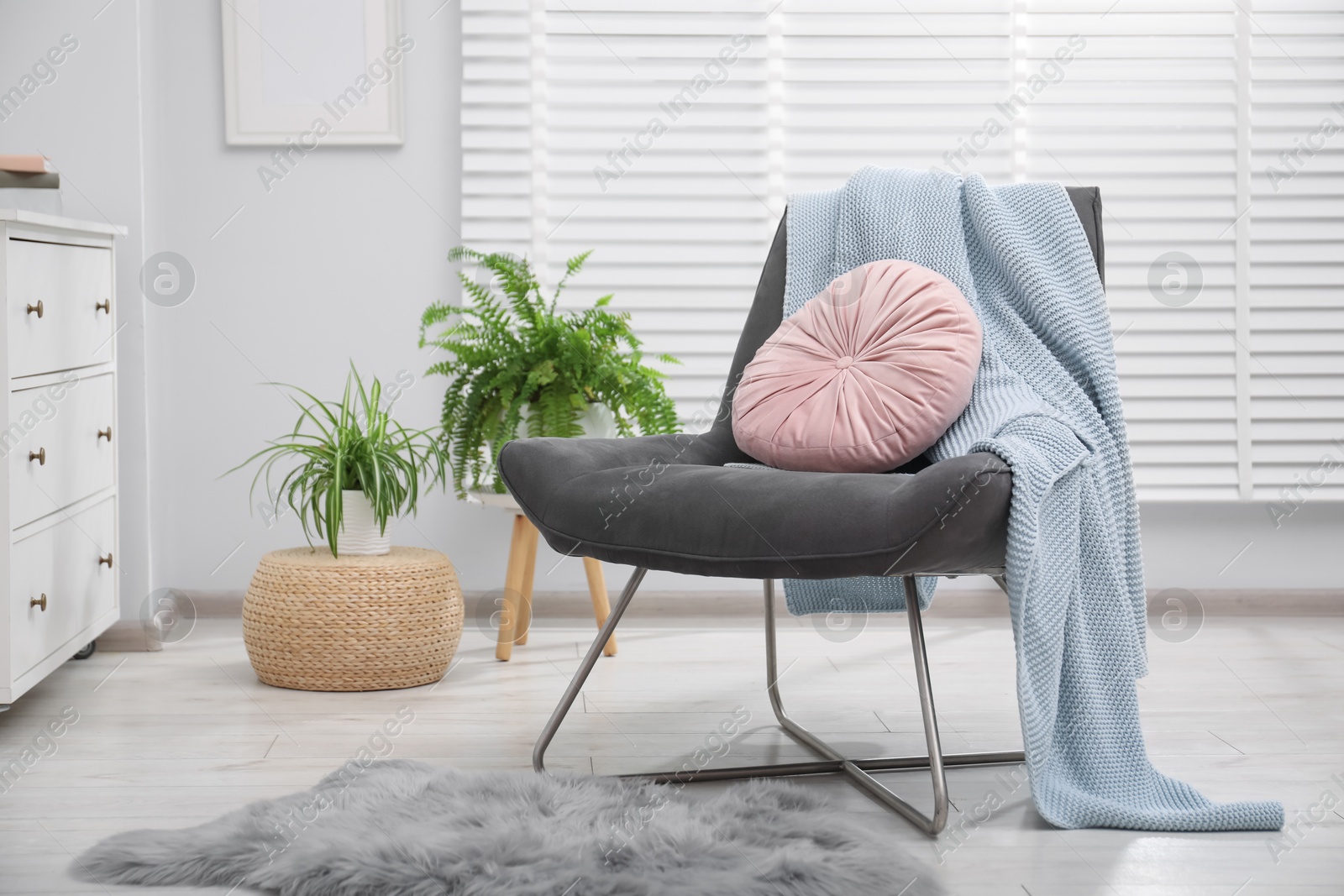 Photo of Comfortable grey armchair with pink pillow and blanket in living room. Interior design