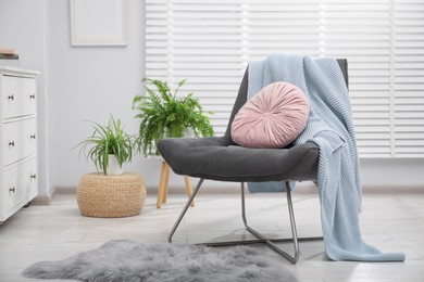Photo of Comfortable grey armchair with pink pillow and blanket in living room. Interior design