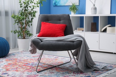 Photo of Comfortable grey armchair with red pillow and blanket in living room. Interior design